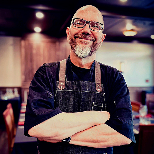 A picture of Chef D'arcy Letourneau smiling and standing with arms crossed in the Kilmorey Restaurant.